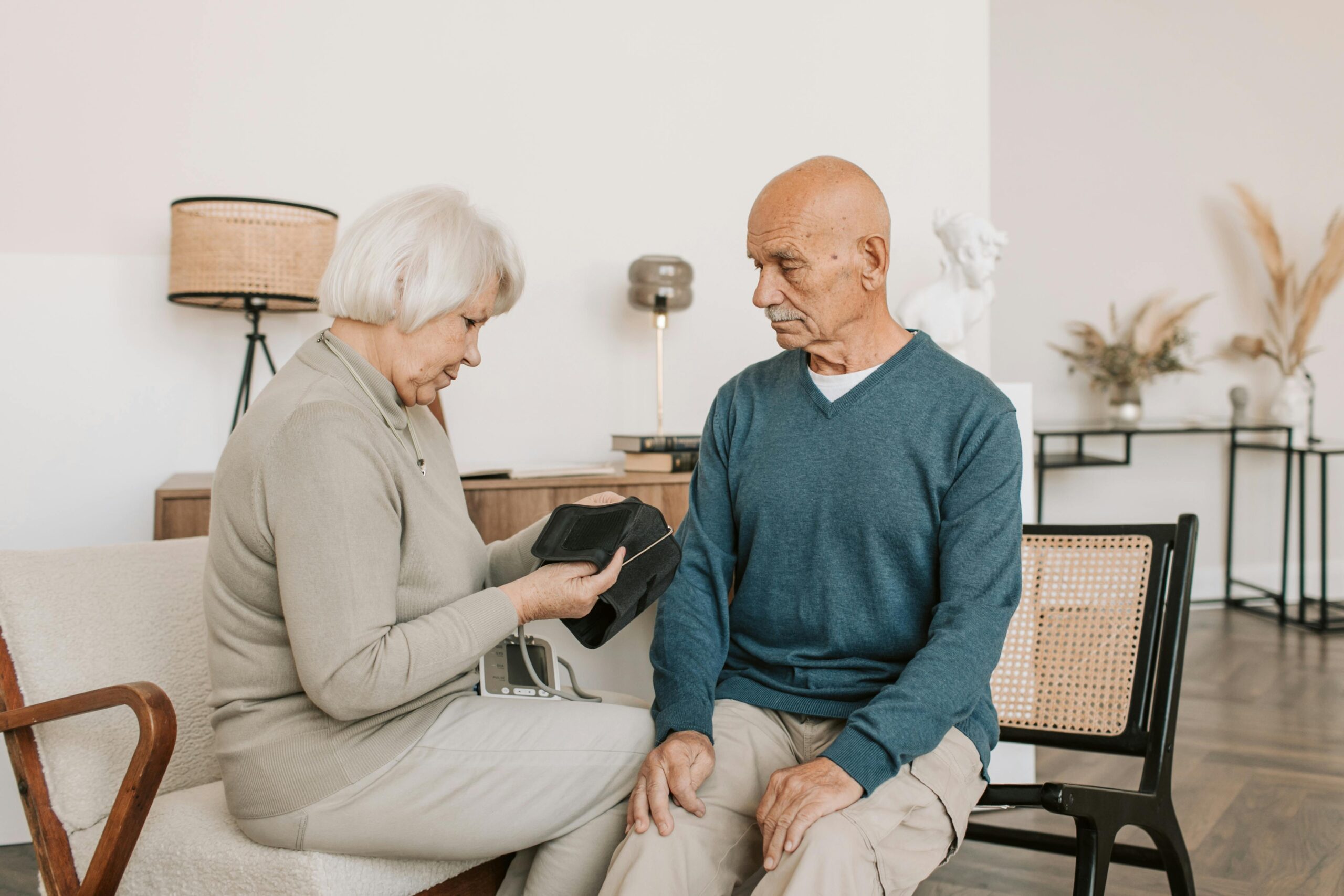 Huyết áp cao: Thời điểm nào cần bắt đầu dùng thuốc? Elderly couple seated together, checking blood pressure with a sphygmomanometer indoors.